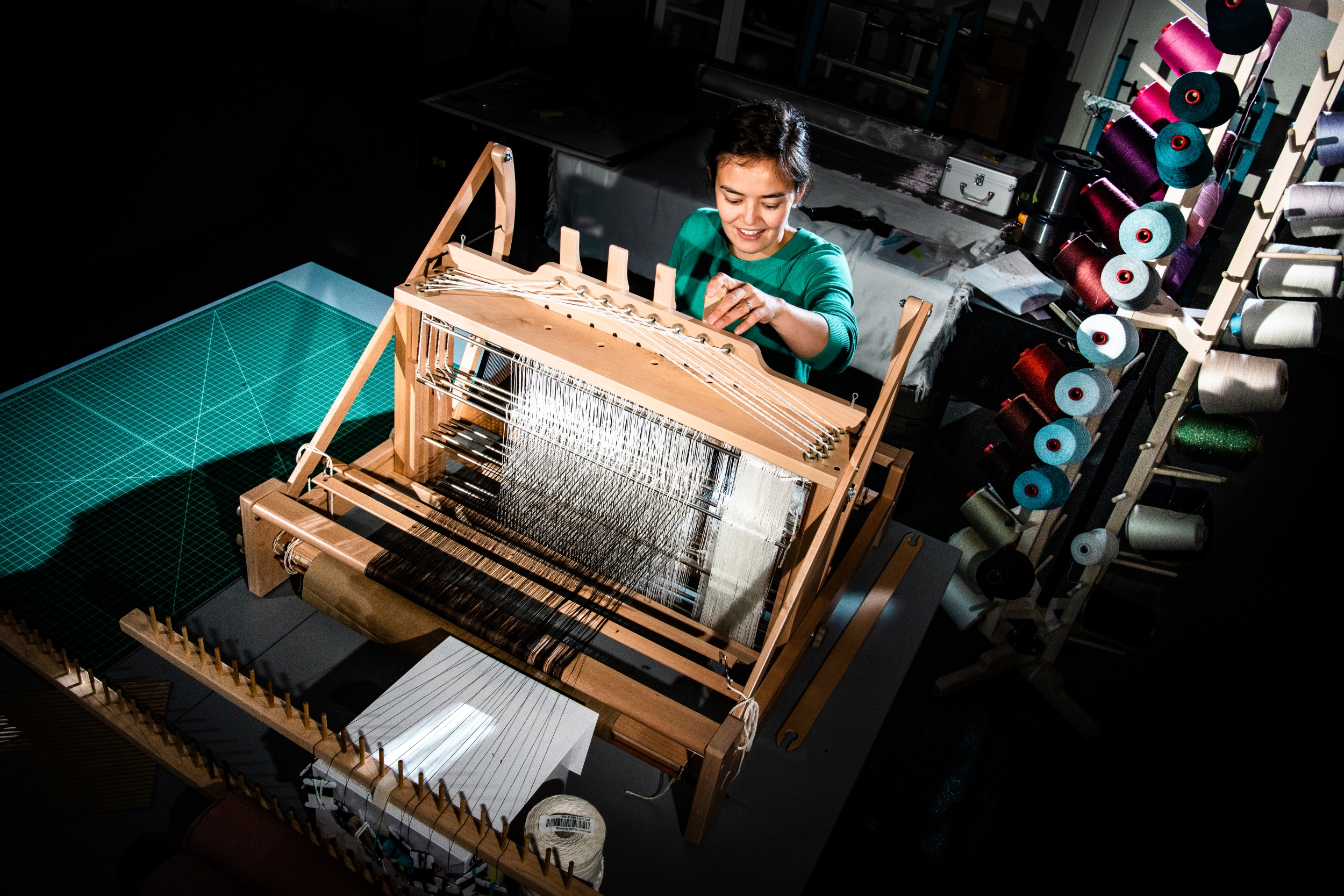 A women stands in front of a fabric weaver 