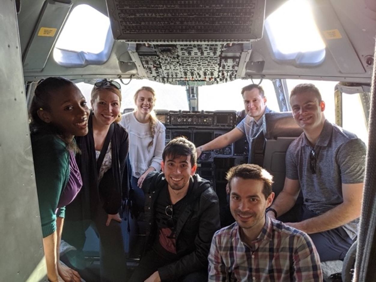 A group of seven people pose for a photo inside the cockpit of a C-17 aircraft. 