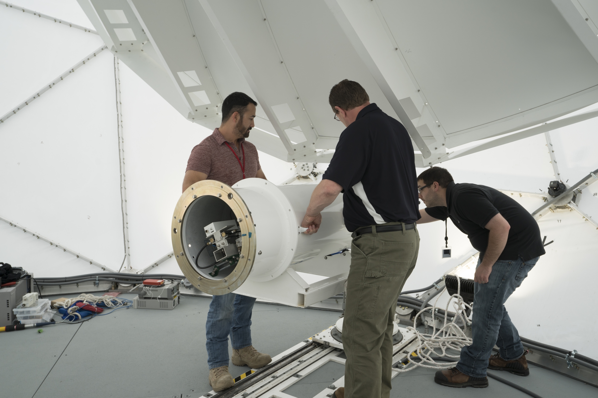 Three individuals install a new antenna feed during the initial MBTT installation.