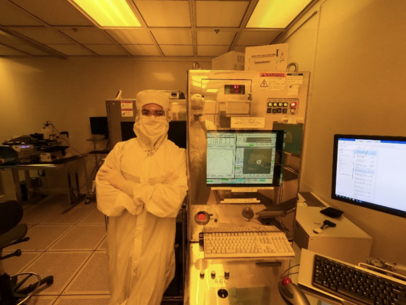 an intern dressed in a "bunny suit" leans against a machine in the microelectronics laboratory.