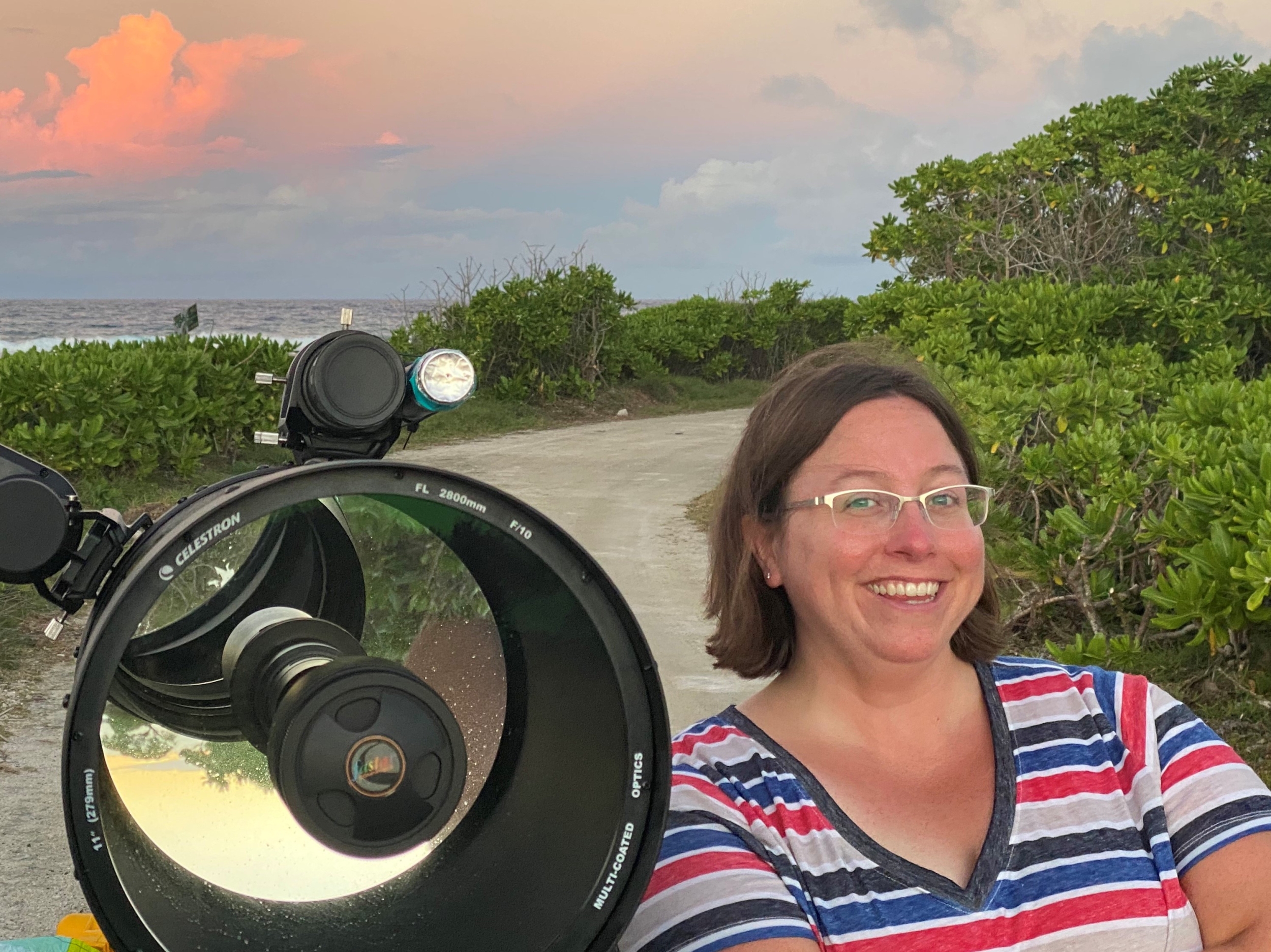 A woman stands in front of a telescope. 