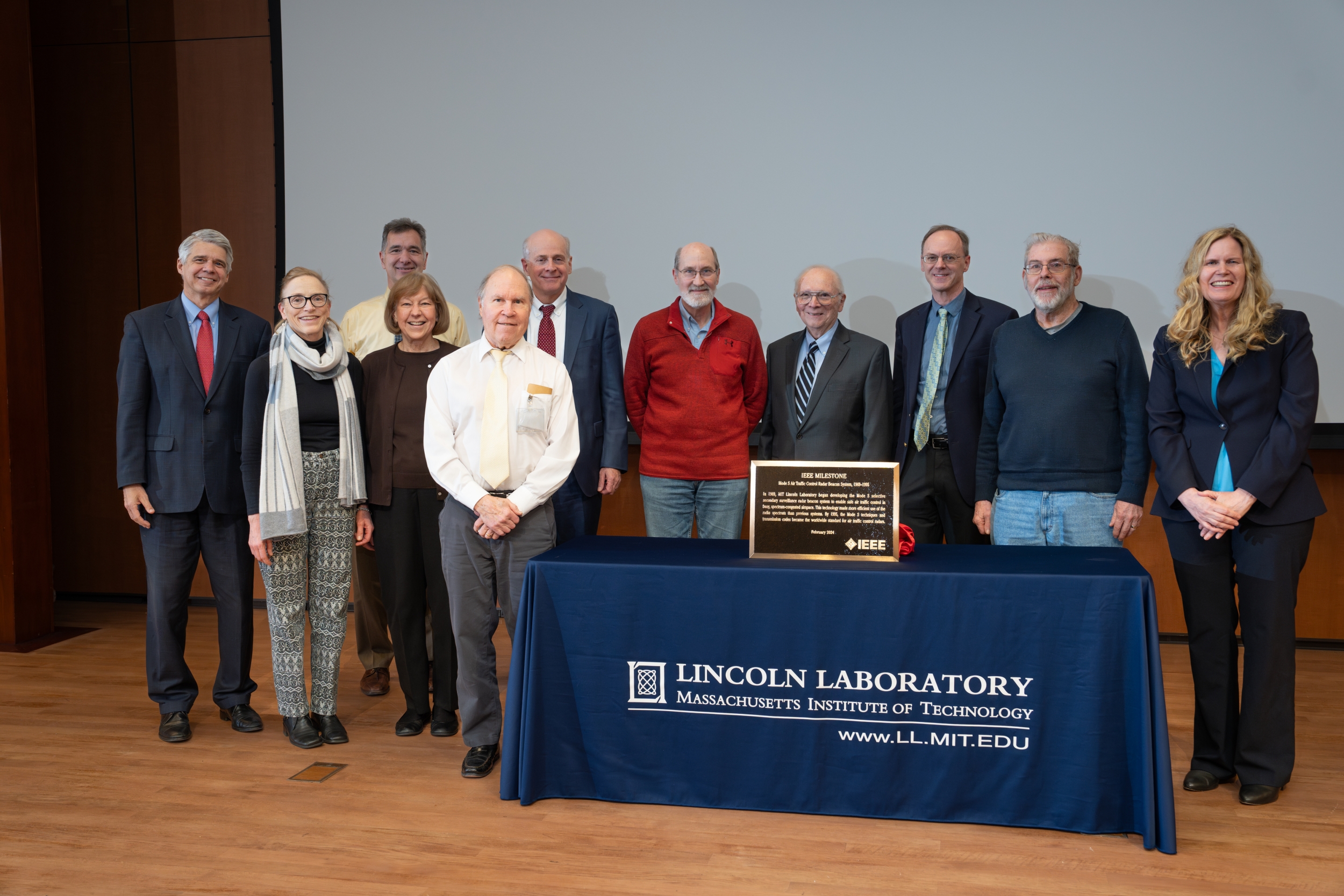 a group photo of people surrounding a table with the Mode S IEEE plaque on it. 