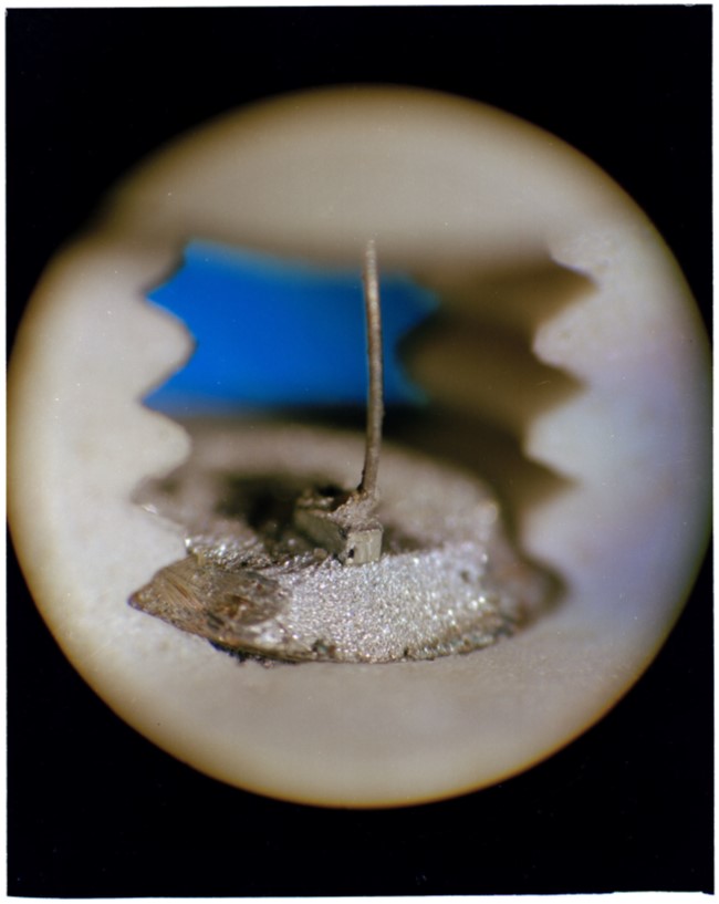 A close-up photo of a semiconductor laser – it shows a tiny block of a metallic material, with a wire attached to it.