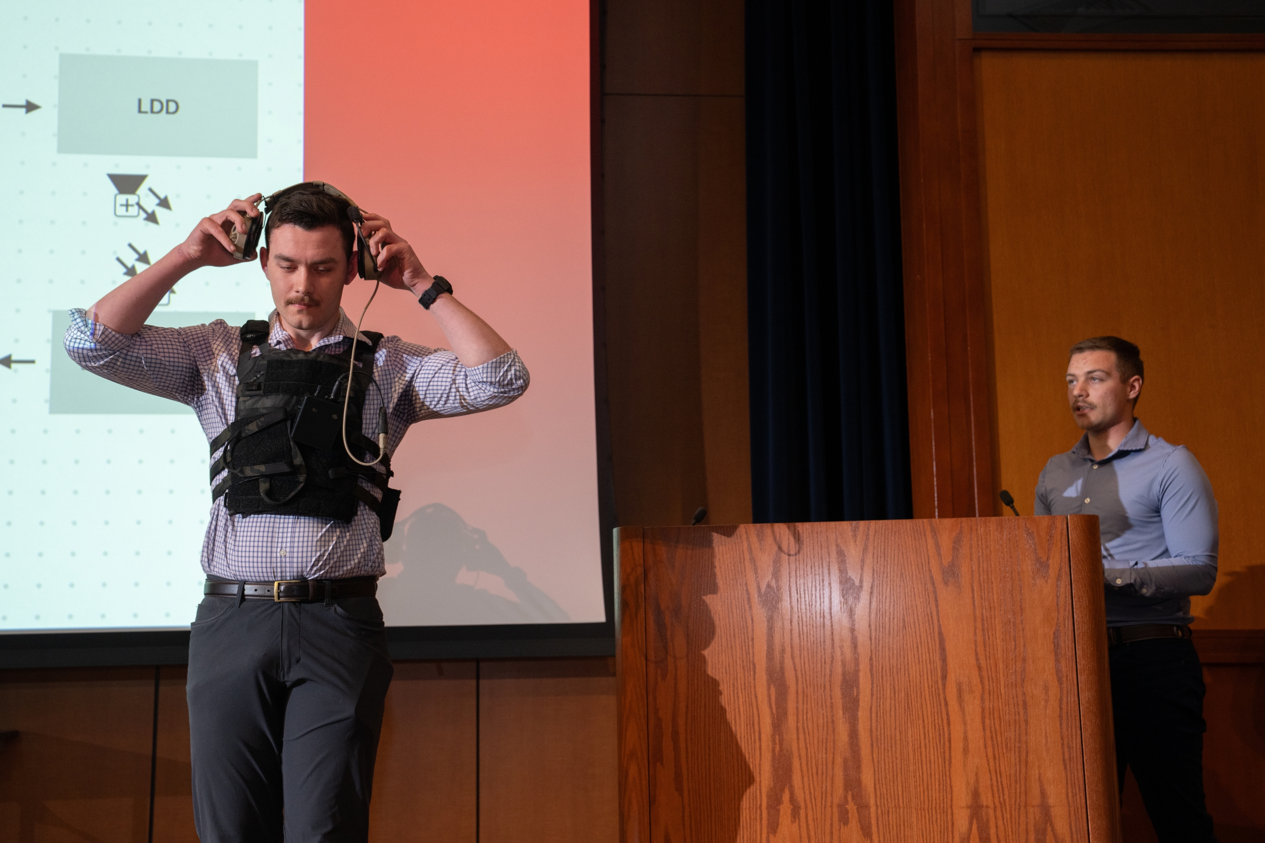 A cadet demonstrates a headset radio on stage.