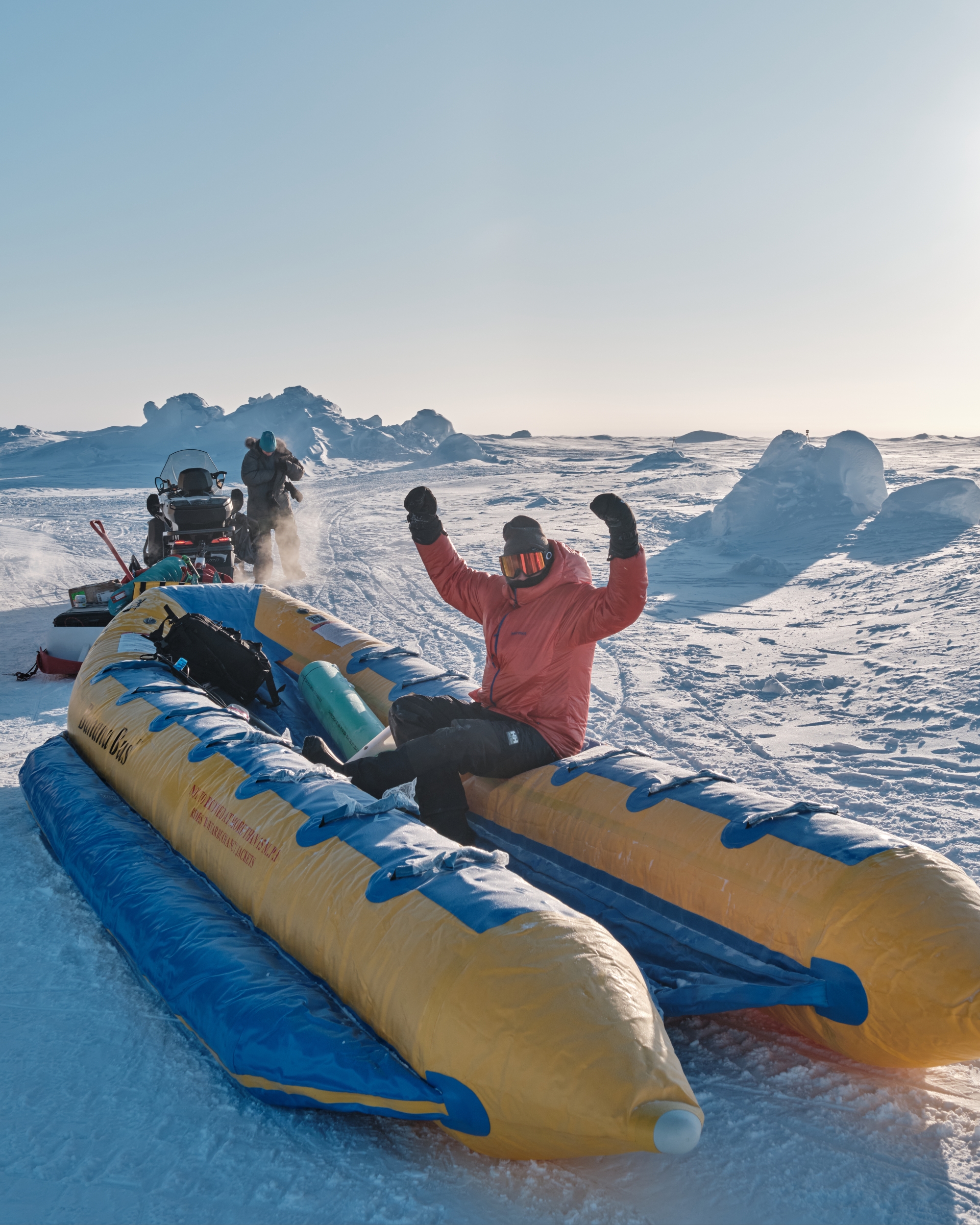 A person rides on a slide towed by a snowmobile. 