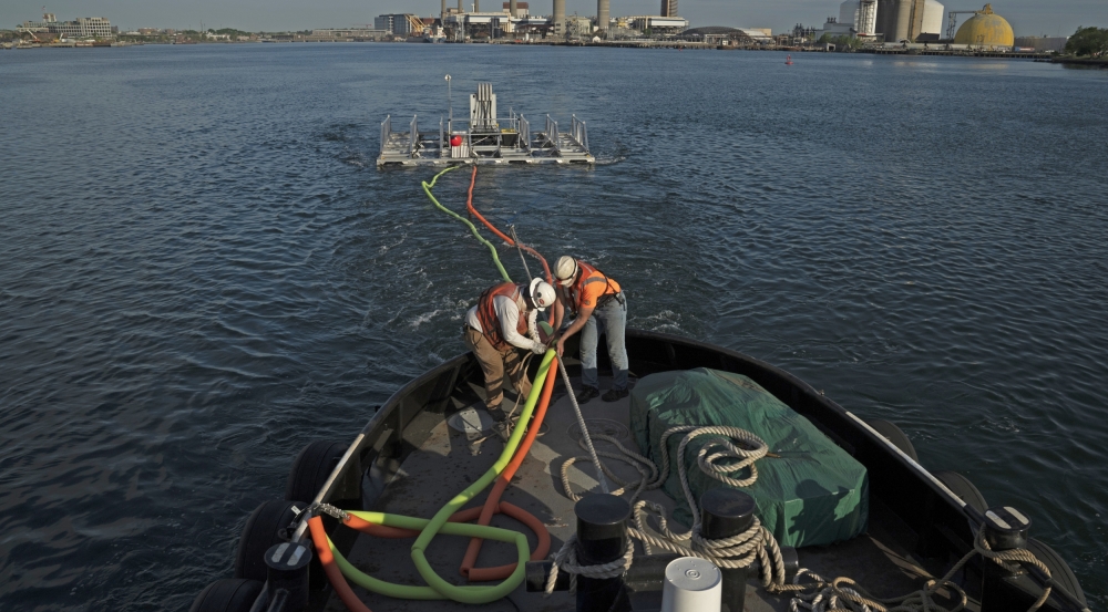 researchers on a boat in boston harbor, with a equipment trailing behind them in the water.