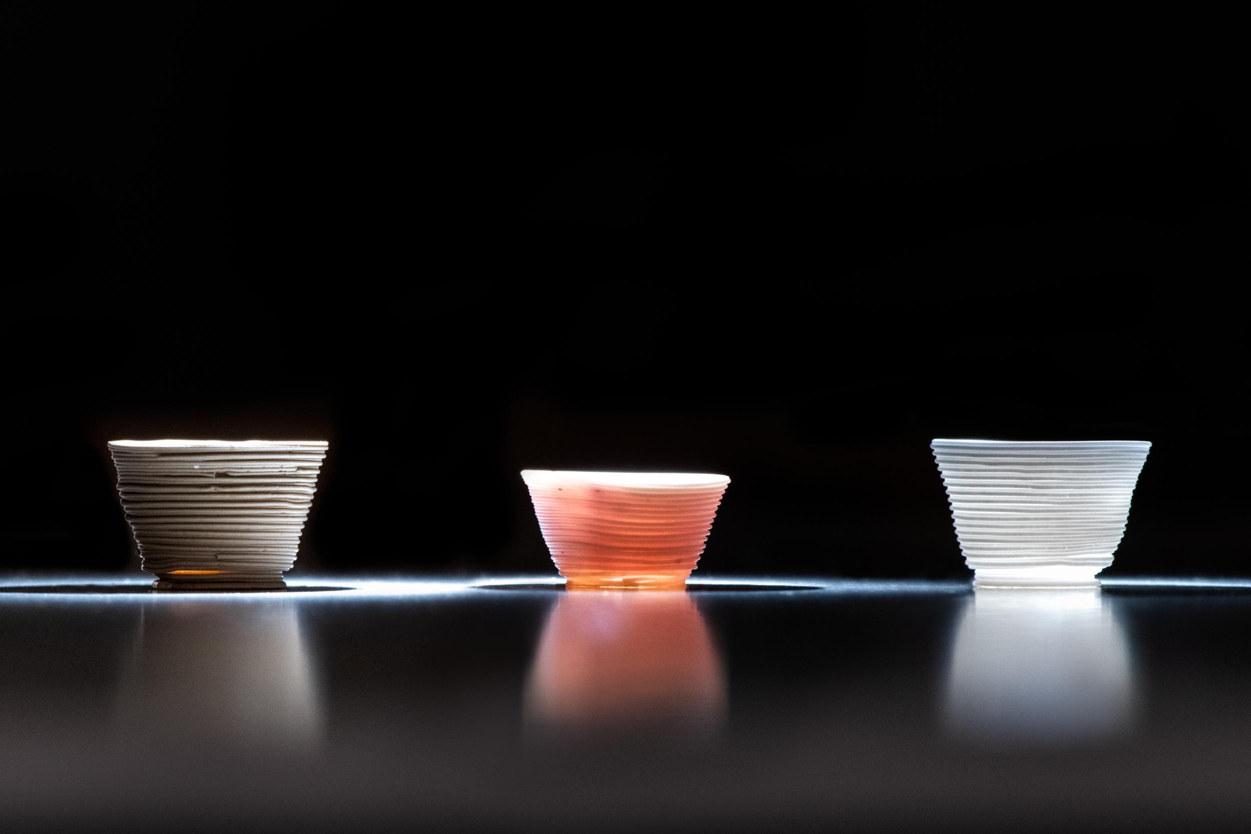 A photo of three 3D-printed glass cups, each a different color.