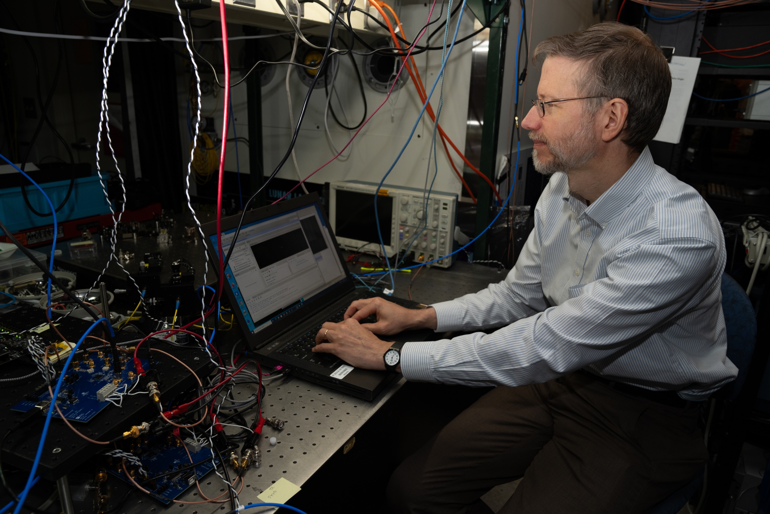 a researcher sits at a laptop in front of a quantum test bed.