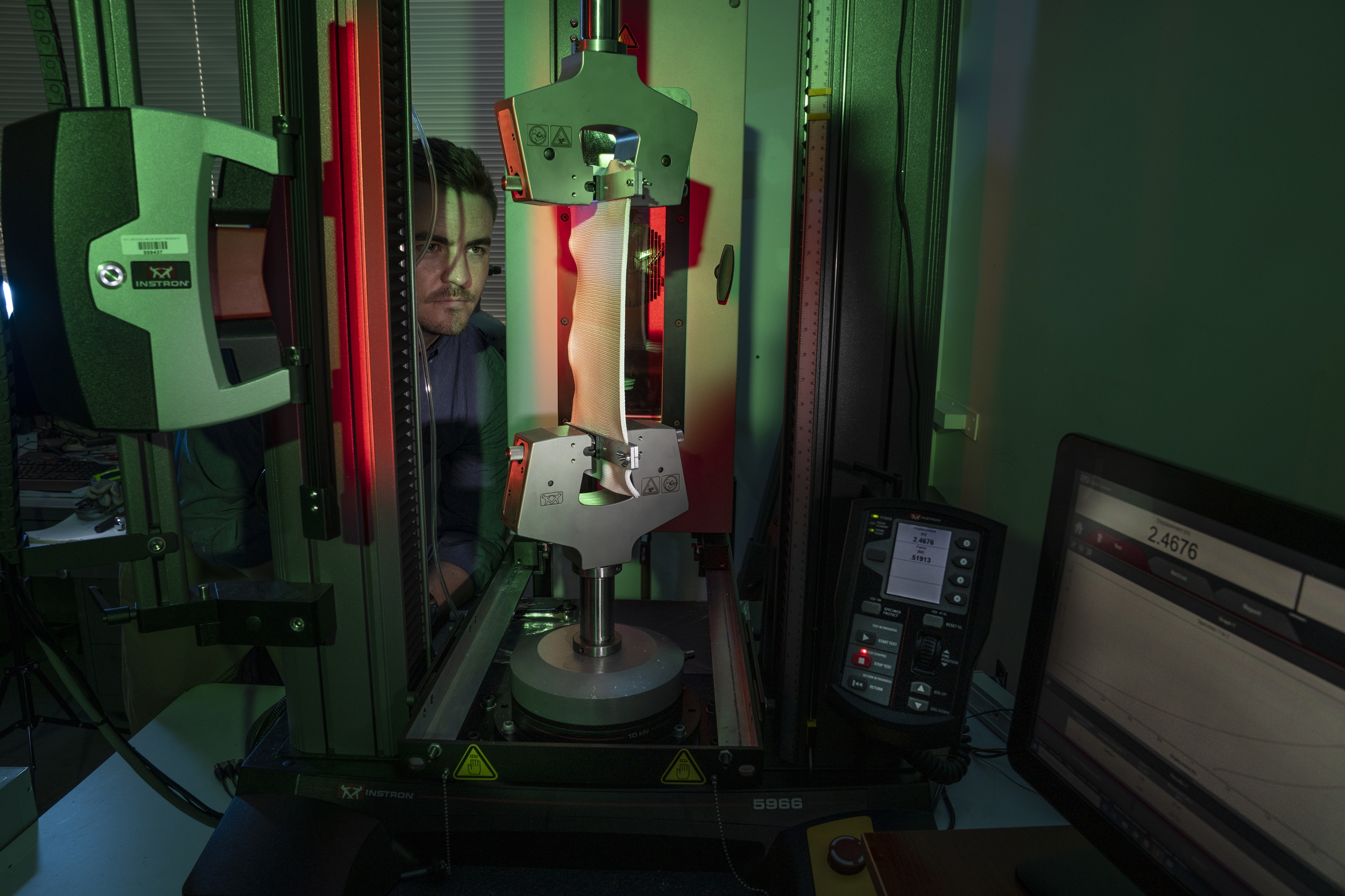 A researcher looking closely at a fabric-looking material being stretched in a machine.