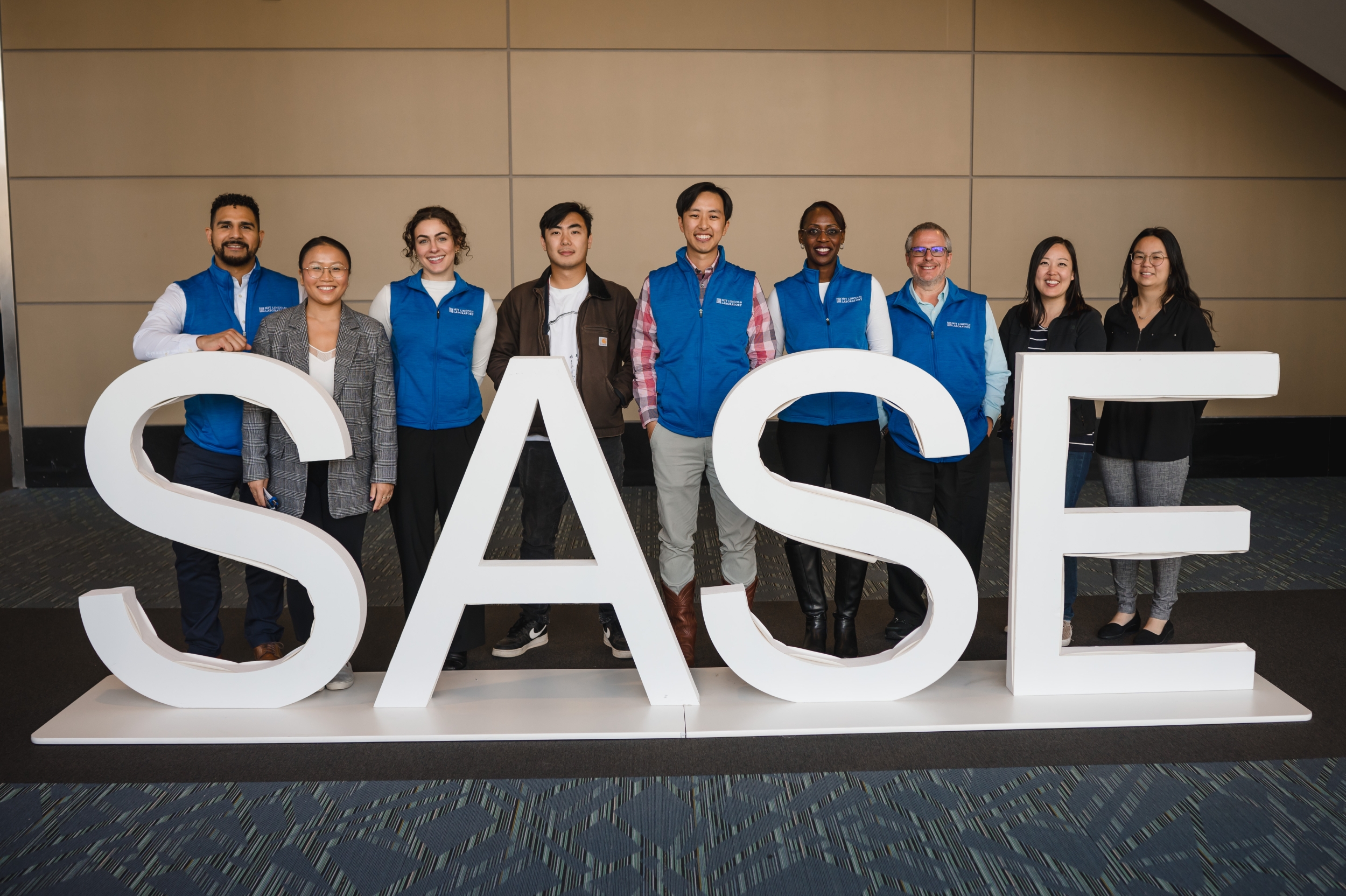 Lincoln Laboratory staff membersstand in front of the SASE logo for a photo at the conference. 