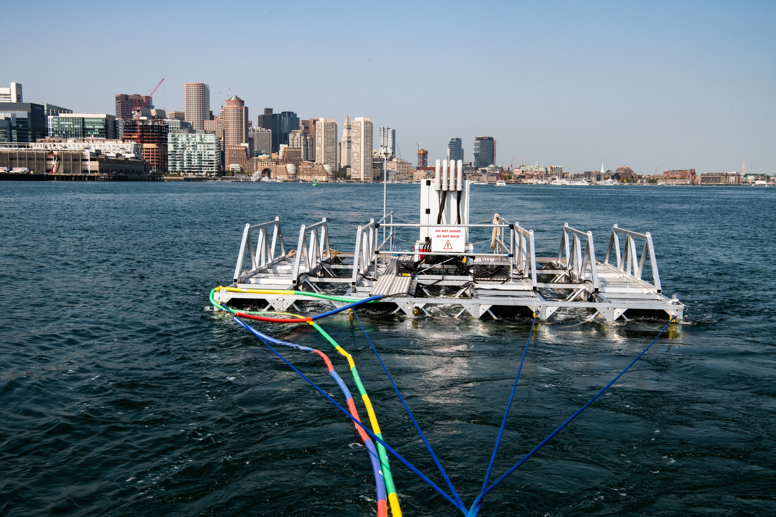 A metal frame floats in Boston Harbor, with the city in the backdrop. 