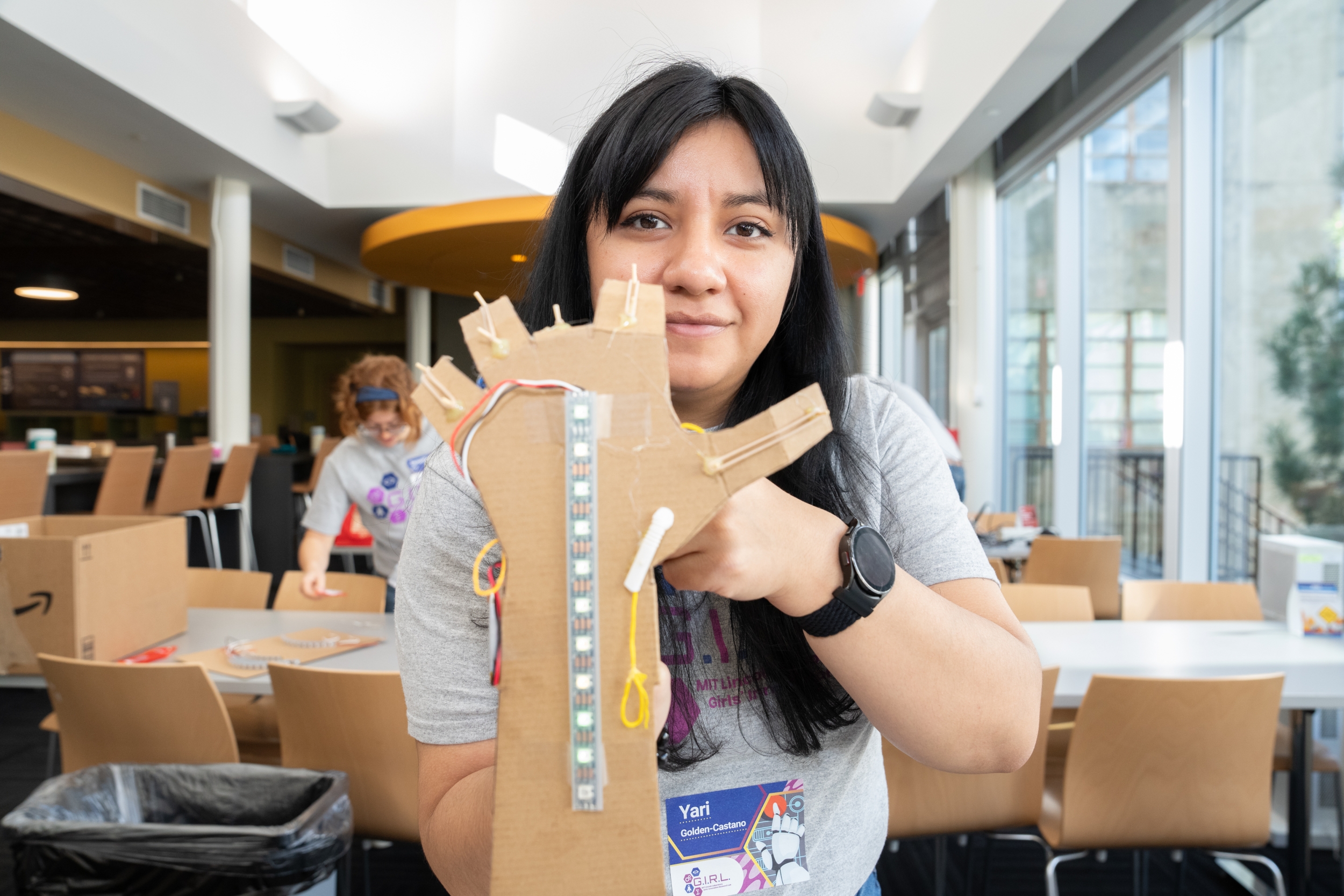 A woman holds a mechanical arm made out of cardboard. 