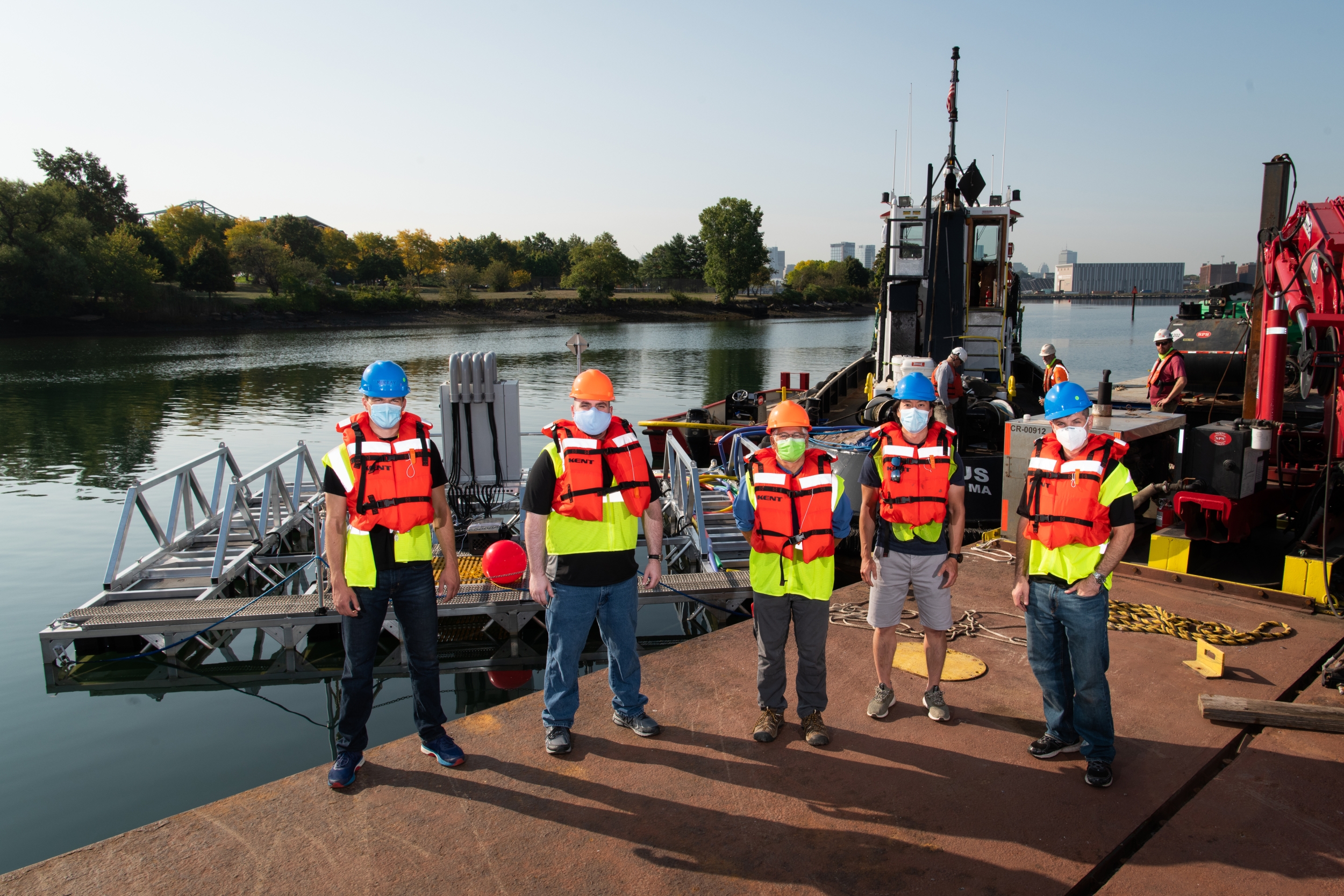 Five individuals stand next to a metal frame hosting a sonar array test bed in Boston Harbor.