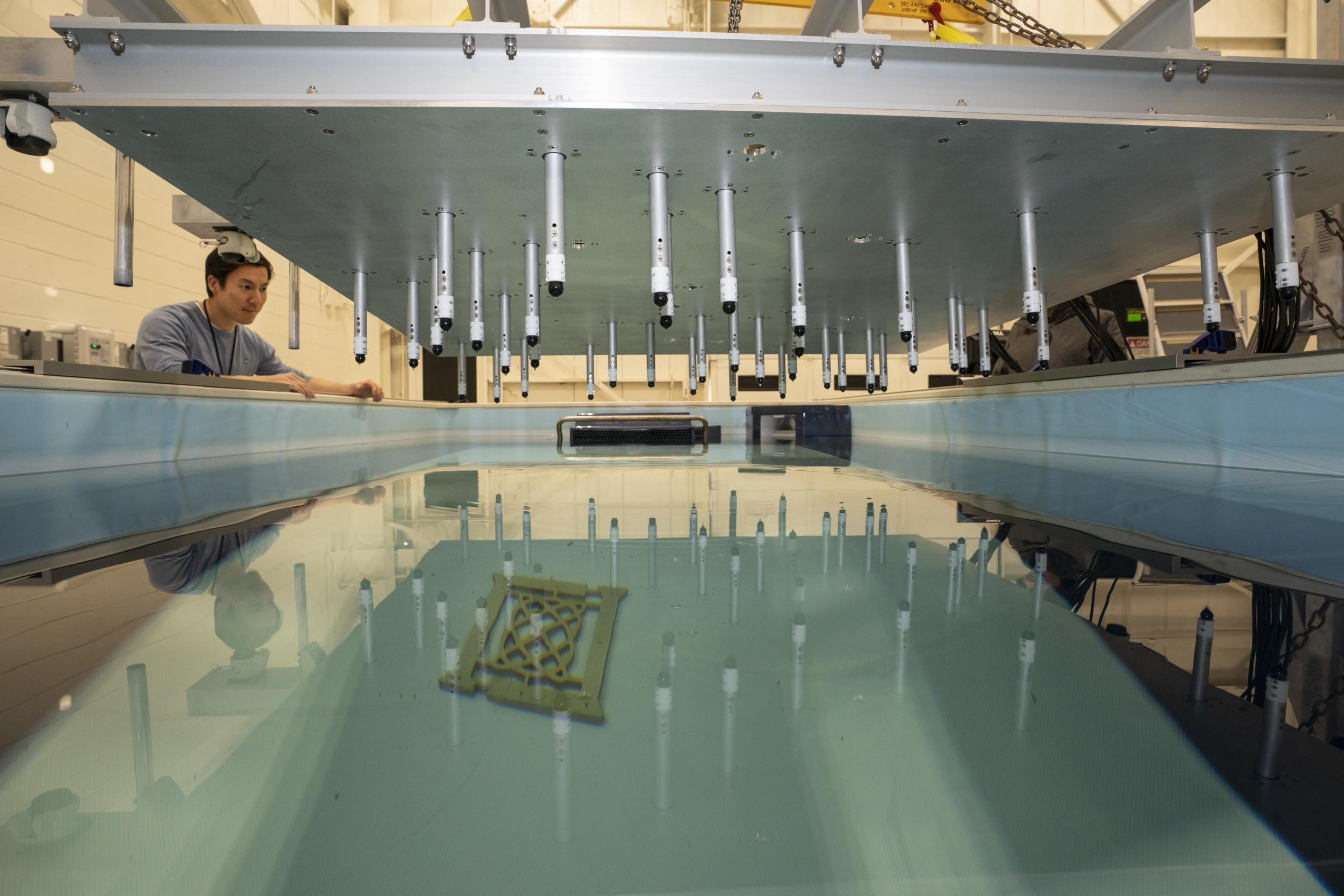 A person examines a sonar array suspended above a test tank. A Lincoln Laboratory logo is positioned near the bottom of the tank.