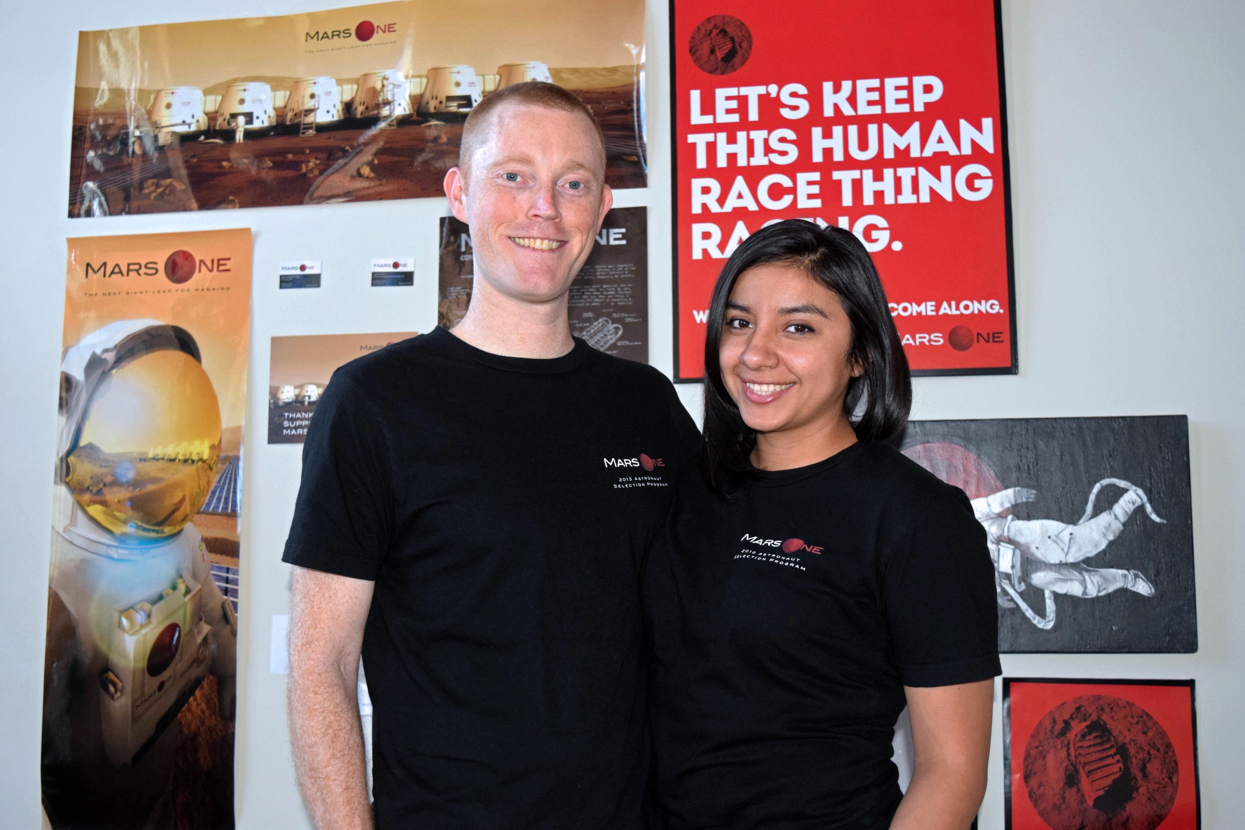 A husband and wife stand together in front of Mars One promotional posters.