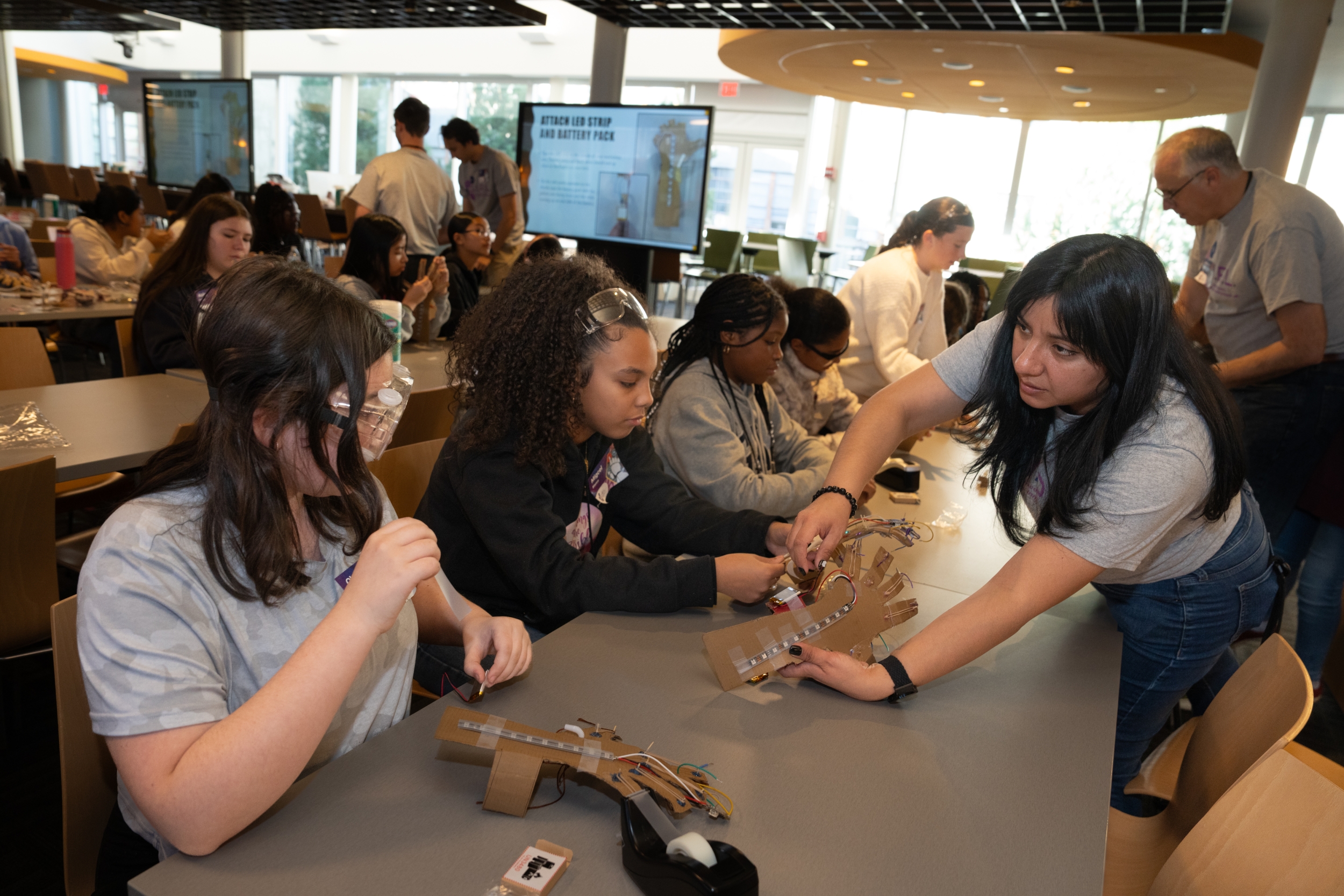 A woman shows a girl how to attach a light strip and battery pack to a mechanical arm.