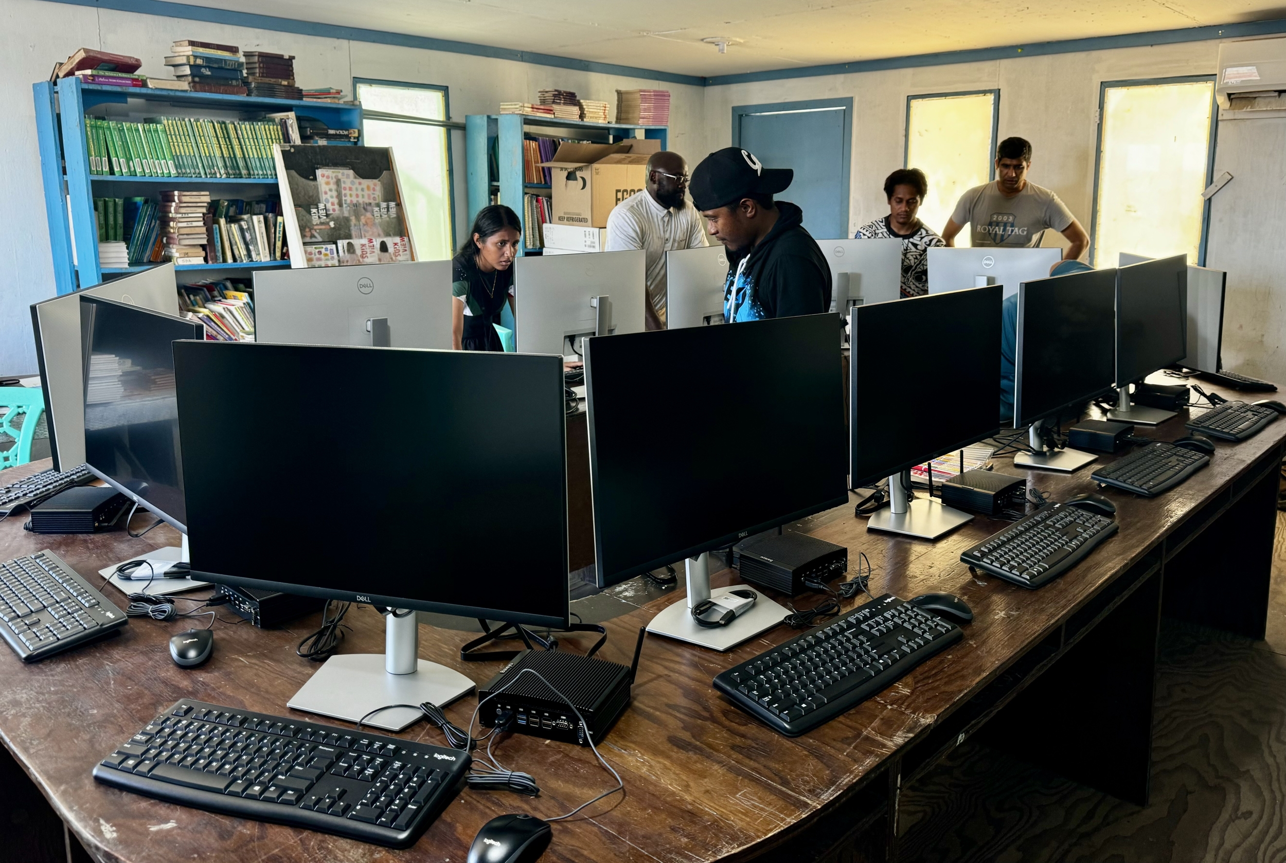 Three interns install 13 computers in a school library as the principal and a pastor observe.