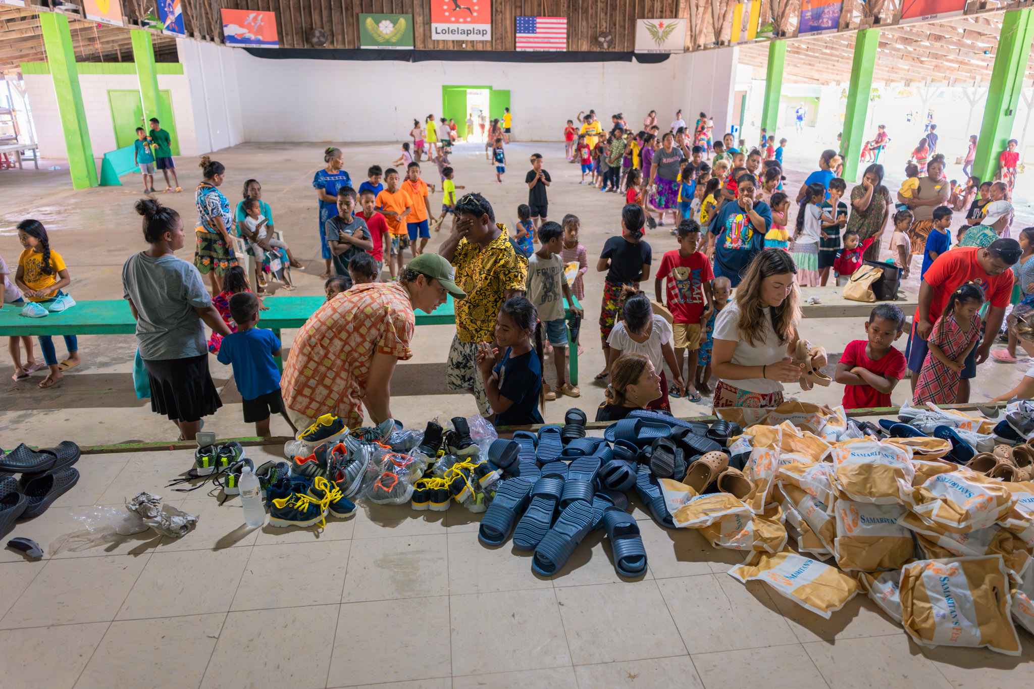 Children and their parents line up in a pavilion to receive shoes during a shoe drive. 