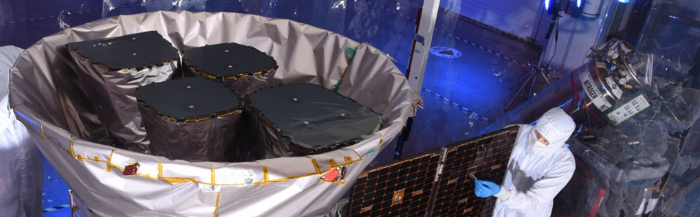 A photo of two scientists inspecting the tess satellite in a cleanroom environment.