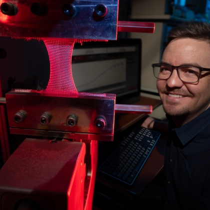 Steve Gillmer is shown smiling next to the industrial knitting machine in red and blue light. 