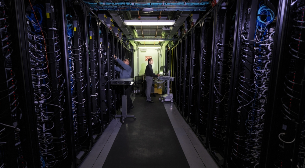 A photo of a hallway between two rows of data center servers. Two researchers are working on the servers.