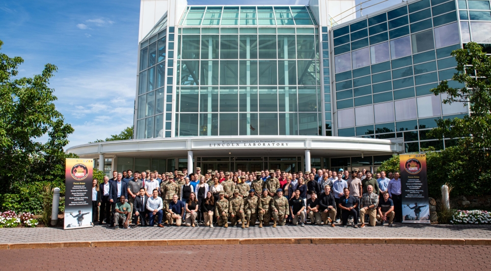  A large group photo of about 100 people in front of the Lincoln Laboratory main entrance.