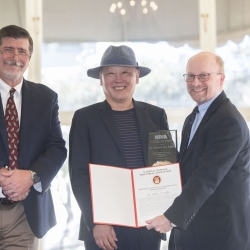 An awardee holds an award plaque next to two award presenters. 