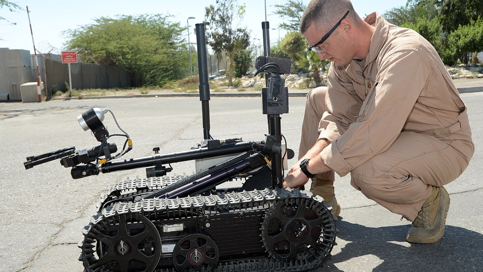 A photo of a service member preparing a small autonomous robot. 