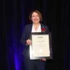 A photograph of Katherine Rink holding a plaque. 