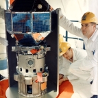 Engineers inspect LES-1 prior to its 1965 launch. The satellite is positioned atop a Titan III rocket on the launch pad at Cape Kennedy, Florida.